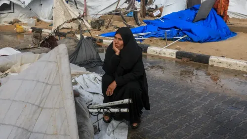 امرأة ترتدي الحجاب تجلس على الأرض وسط خيام مدمرة ومياه راكدة، تعكس معاناة سكان غزة خلال العواصف الشتوية.