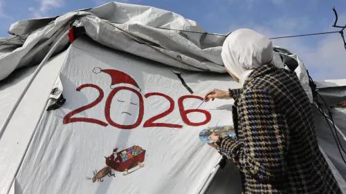 امرأة ترتدي حجابًا ترسم على خيمة تحمل الرقم "2026"، تعبيرًا عن الأمل في ظل الظروف الصعبة في غزة.