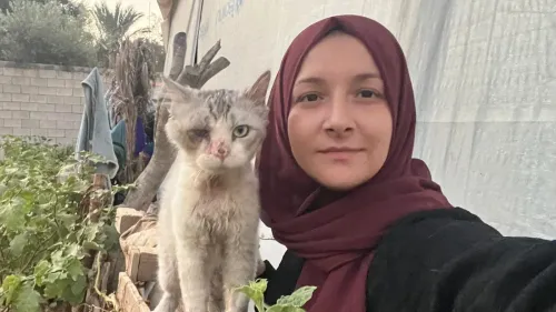 امرأة ترتدي حجابًا بنيًا، تلتقط سيلفي مع قطة ذات عين واحدة، في خلفية خضرة وأشجار، تعكس الأمل في ظروف صعبة.