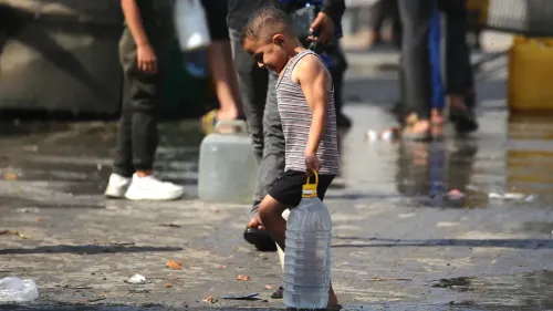 طفل صغير يحمل زجاجة مياه في منطقة مغمورة بالمياه، مما يعكس أزمة نقص المياه الحادة في غزة بسبب الحرب والحصار.