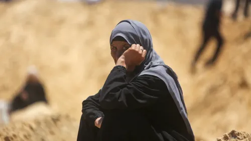 امرأة فلسطينية ترتدي الحجاب، تجلس على الأرض في منطقة صحراوية، تعكس ملامح وجهها القلق والمعاناة وسط الأوضاع الصعبة في غزة.