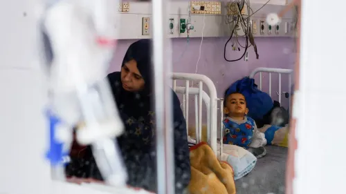 امرأة فلسطينية تجلس بجانب طفل مريض في مستشفى بغزة، يعكسان معاناة المرضى بسبب القيود الإسرائيلية على الرعاية الطبية.