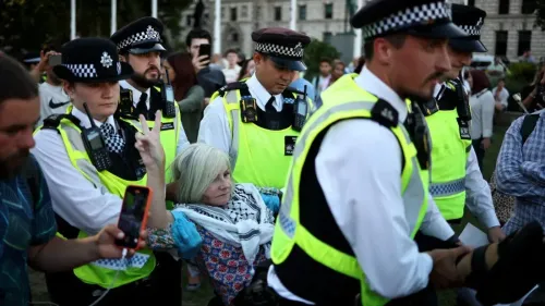 اعتقال امرأة مسنّة خلال احتجاج، حيث تحيط بها الشرطة وتظهر على وجهها ملامح التعب، مع وجود متظاهرين آخرين في الخلفية.