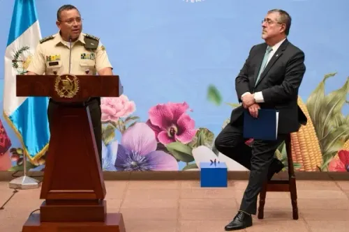 اجتماع رسمي في غواتيمالا سيتي حيث يتحدث مسؤول أمني عن قانون مكافحة العصابات الجديد، مع وجود الرئيس أريفالو في الخلفية.