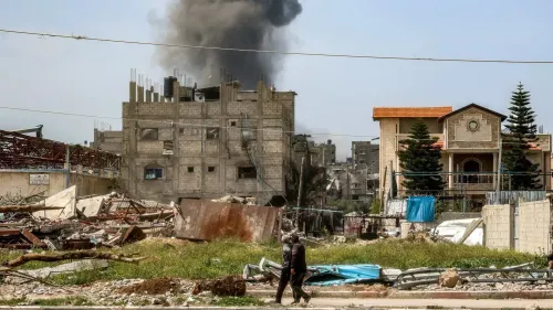 دخان أسود يتصاعد من مبنى مدمر في غزة، مع وجود أشخاص يسيرون بين الأنقاض، مما يعكس آثار الغارات الجوية الإسرائيلية.