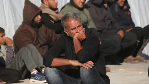 رجل يجلس على الأرض في غزة، يبدو عليه القلق والتفكير، بينما خلفه مجموعة من الرجال يجلسون في انتظار. تعكس الصورة التوتر والضغط في سياق المفاوضات السياسية.