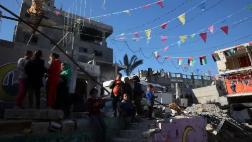 أطفال وشباب يجتمعون في منطقة مدمرة في غزة، مع زينة ملونة تعكس أجواء الاحتفال رغم الظروف الصعبة.