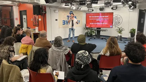 اجتماع في منتدى الشعب في نيويورك، حيث يتحدث ناشط حول حملة ، مع عرض تقديمي خلفه يناقش دور مجموعة تاتا في العلاقات الهندية الإسرائيلية.