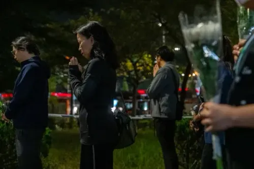 مجموعة من الأشخاص يقفون في حديقة ليلاً، بعضهم يحمل زهوراً، في لحظة تأمل وصلاة تأبين لضحايا حريق تاي بو في هونغ كونغ.