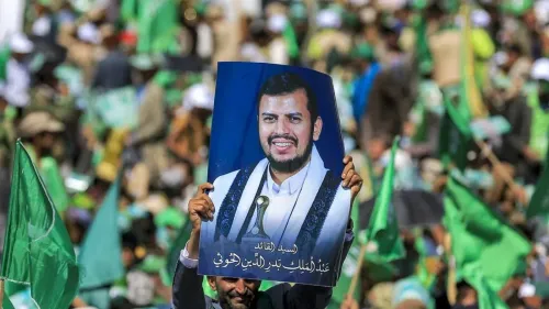 مؤيد يحمل صورة لعبد الملك الحوثي وسط حشد من الناس، مع أعلام خضراء ترفرف في الخلفية، خلال تجمع حاشد في اليمن.
