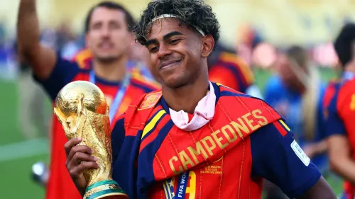 لامين يمال يحمل كأس العالم بفخر بعد فوز إسبانيا، مع وشاح "CAMPEONES" يعكس إنجازاته الرياضية والهوية المتعددة الثقافات.