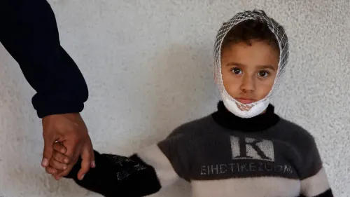 طفل مصاب برباط على رأسه، يمسك بيد شخص بالغ، يعكس معاناة الأطفال في غزة بسبب النزاع المستمر والحاجة الملحة للإجلاء الطبي.