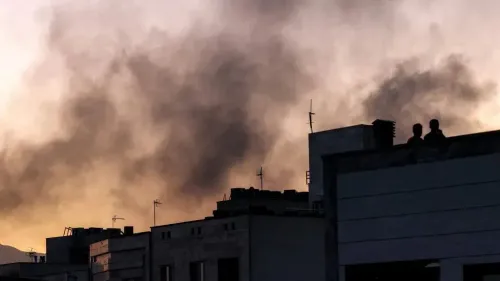 دخان كثيف يتصاعد في السماء خلال غروب الشمس، بينما يظهر شخصان على سطح مبنى، مما يعكس تأثير الضربات الإسرائيلية في إيران.
