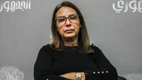 امرأة ترتدي نظارات وتظهر تعبيراً جدياً، وهي تجلس أمام خلفية رمادية، تعكس أجواء القلق بشأن قضايا حقوق الإنسان في تونس.