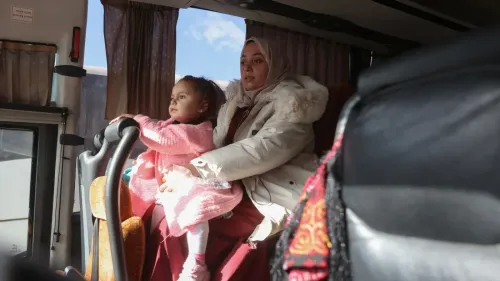 امرأة ترتدي معطفًا أبيض تجلس في حافلة مع طفلة صغيرة ترتدي سترة وردية، تعكس لحظة من الانتقال والأمل بعد الصراعات في غزة.