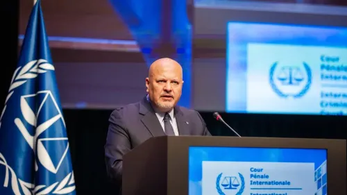 تظهر الصورة المدّعي العام كريم خان أثناء إلقاء خطاب في المحكمة الجنائية الدولية، مع شعار المحكمة في الخلفية.
