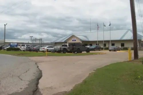 مركز احتجاز في لويزيانا، حيث تتجمع سيارات في الساحة، وسط غيوم رمادية، يعكس قضايا احتجاز النساء الحوامل.