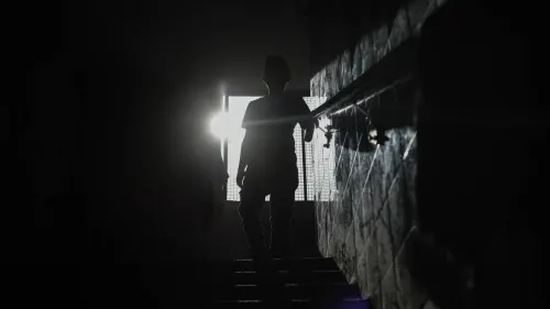 شخص يقف في الظلام أمام نافذة مضاءة، يعكس تحديات انقطاع الكهرباء في غزة وتأثيره على الحياة اليومية.