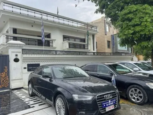مبنى سكني في نيودلهي يحمل أعلام دولية، مع سيارة فاخرة متوقفة أمامه، في سياق تحقيقات الشرطة حول سفارة وهمية.
