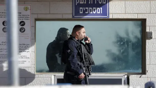 شرطي إسرائيلي مسلح يقف أمام نافذة زجاجية، مع وجود لافتة تشير إلى مركز احتجاز، في سياق مناقشة مشروع قانون عقوبة الإعدام للأسرى الفلسطينيين.