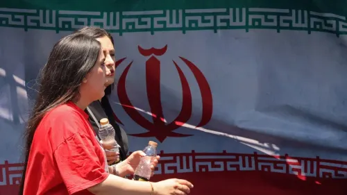 امرأتان تسيران أمام علم إيران، يحملن زجاجات مياه، تعبيراً عن الأمل في تحقيق اتفاق سلام بين إيران والولايات المتحدة.