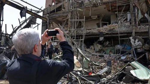 رجل يلتقط صورة لهدم مبنى متضرر، مع ظهور حطام وبقايا مواد بناء، في سياق الأحداث العسكرية الأخيرة في إيران.