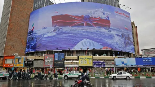 صورة لافتة إعلانية ضخمة تظهر ناقلة نفط حمراء في البحر، مع زوارق حراسة بالقرب منها، تعكس التوترات البحرية في الخليج.