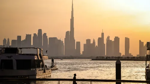أفق مدينة دبي عند الغروب، يظهر برج خليفة كأعلى نقطة في الأفق، مع قوارب راسية على الواجهة المائية، مما يعكس تأثير الأحداث الأخيرة على الاقتصاد.