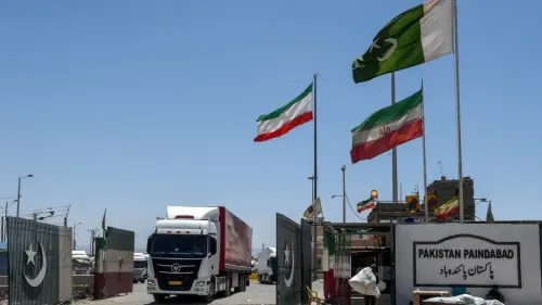مركبة شحن كبيرة تعبر الحدود بين باكستان وإيران، حيث ترفرف الأعلام الإيرانية والباكستانية، مما يرمز إلى تعزيز التجارة بين البلدين.