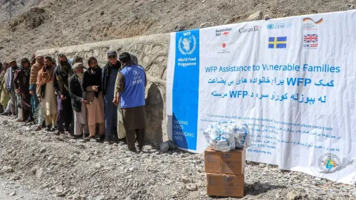 طابور من الأشخاص ينتظرون المساعدات الغذائية من برنامج الأغذية العالمي، مع لافتة توضح الدعم المقدم للعائلات الضعيفة.