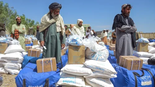 تجمع رجال أفغان في موقع توزيع المساعدات الإنسانية، محاطين بأكياس تحتوي على إمدادات غذائية ومواد ضرورية، وسط أزمة إنسانية متفاقمة.