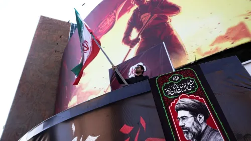 رجل يرفع العلم الإيراني أمام لوحة كبيرة تحمل صورة قيادي في الحرس الثوري، في سياق التصعيد العسكري الإيراني وتحذيراته للأعداء.