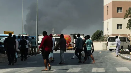 سكان يتجولون في منطقة حضرية، مع تصاعد الدخان في الخلفية نتيجة الغارات الجوية، مما يعكس الوضع المتأزم في الخليج.