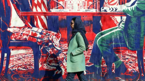 امرأة ترتدي معطفًا أخضر تسير بجانب جدارية ملونة تمثل العلاقات الإيرانية الأمريكية، تعكس التوترات السياسية الحالية.
