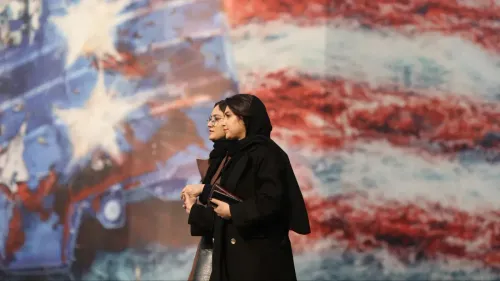 امرأتان ترتديان الحجاب تسيران معًا أمام جدارية ملونة تتضمن ألوان العلم الأمريكي، تعكس الأجواء الاجتماعية والسياسية في إيران.