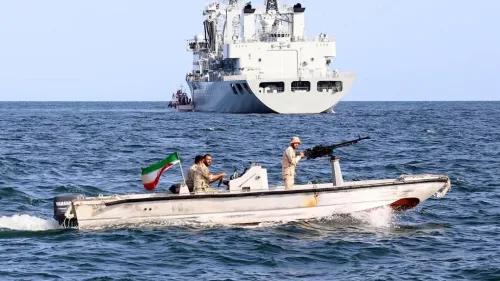 زورق حرس ثوري إيراني مسلح يبحر في الخليج الفارسي مع سفينة حربية كبيرة في الخلفية، يعكس استراتيجية إيران البحرية في مضيق هرمز.