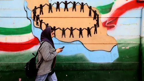 امرأة ترتدي حجابًا تسير بجوار جدارية ملونة تمثل التضامن، مع أشخاص يتشابكون بأيديهم على شكل خريطة إيران.