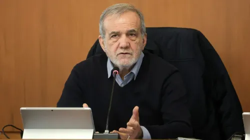 رجل مسن يتحدث في اجتماع، مع جهاز كمبيوتر محمول أمامه، في سياق مناقشات حول الوضع الاقتصادي والسياسي في إيران.