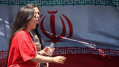 امرأتان تسيران أمام علم إيران، تعبران عن مشاعر مختلطة من الارتياح والقلق بعد إعلان اتفاق لوقف الحرب.