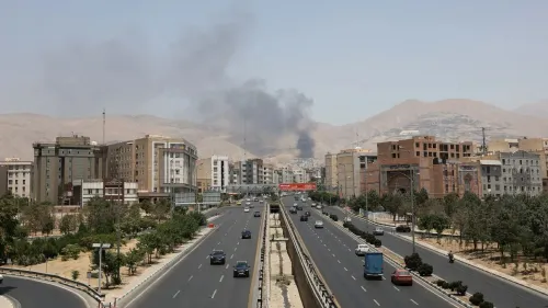 دخان يتصاعد من منطقة سكنية في طهران بعد سقوط صاروخ إسرائيلي، مع وجود سيارات على الطريق وأبنية محيطة.