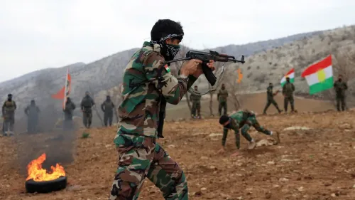 مقاتل كردي يرتدي زيًا عسكريًا ويحمل سلاحًا، بينما يشارك آخرون في تدريبات عسكرية في منطقة جبلية، مع أعلام كردية تتواجد في الخلفية.