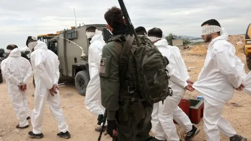 أفراد فلسطينيون مقيدون ومعصوبو الأعين يرتدون ملابس بيضاء، برفقة جندي إسرائيلي مسلح، في سياق اتهامات بانتهاكات حقوق الإنسان.