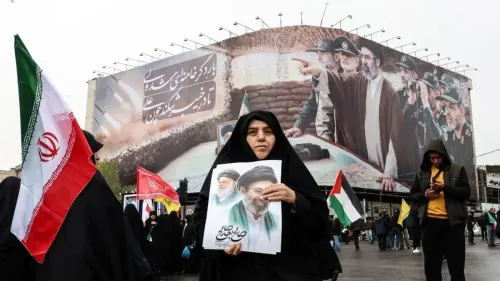 امرأة ترتدي الحجاب تحمل صورة لزعيم إيراني، بينما تلوح بعلم إيران في تجمع حاشد، مع خلفية لملصق كبير يظهر شخصيات سياسية وعسكرية.