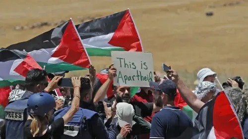 محتجون فلسطينيون يحملون الأعلام ويعرضون لافتة مكتوب عليها "هذا فصل عنصري"، مع خلفية طبيعية في منطقة مفتوحة.