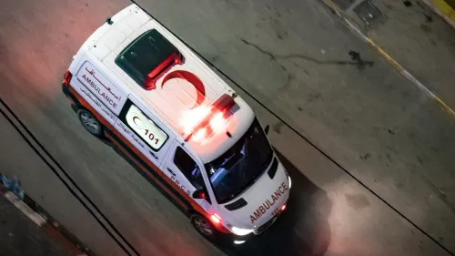 سيارة إسعاف فلسطينية تسير في الشارع، مع أضواء الطوارئ مضاءة، تعكس الحاجة الملحة للعلاج الطبي للأطفال المصابين بالسرطان.