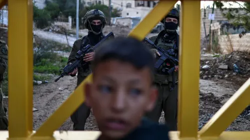 طفل فلسطيني يظهر في المقدمة مع جنود إسرائيليين مسلحين في الخلفية، مما يعكس التوتر والتهديدات التي يواجهها الأطفال في الضفة الغربية.