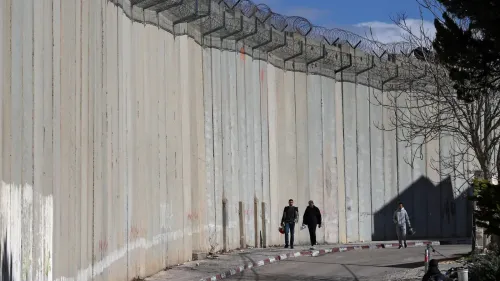 عمال فلسطينيون يسيرون قرب جدار الفصل في الضفة الغربية، حيث يحاولون عبور الجدار بحثاً عن عمل في القدس، وسط توترات متزايدة.