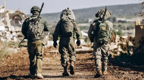 جنود إسرائيليون يسيرون في منطقة مدمرة، يحملون أسلحتهم وحقائبهم، في سياق التوترات المستمرة بين إسرائيل وحزب الله.