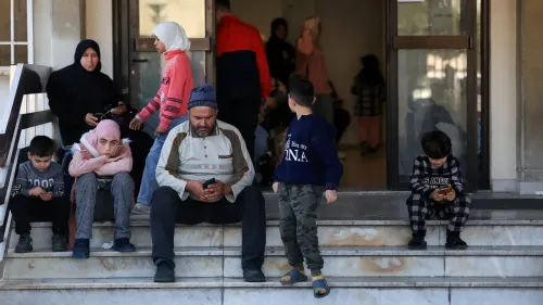 عائلات نازحة تجلس على درجات مبنى، تعبيرات القلق واضحة على وجوههم، في ظل التصعيد العسكري في جنوب لبنان.