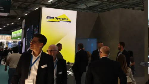 وفد زوار في معرض دفاعي أمام شعار شركة Elbit Systems الإسرائيلية المتخصصة في الطائرات المسيّرة وأنظمة المراقبة.